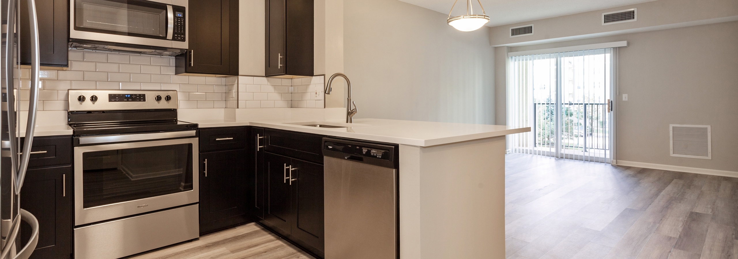 AMLI at Seven Bridges living room and kitchen with dark cabinetry and stainless steel appliances and wood-style plank floors