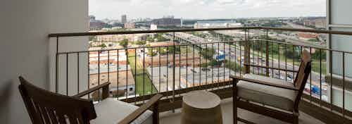 Daytime exterior view of AMLI Design District apartment balcony with two chairs and small table overlooking the city