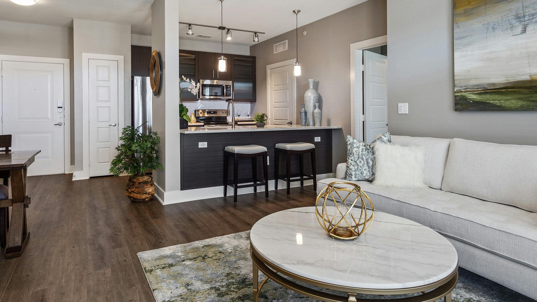 Living room at AMLI South Shore with dark hardwood and light walls with a white sofa and view of stools at kitchen counter