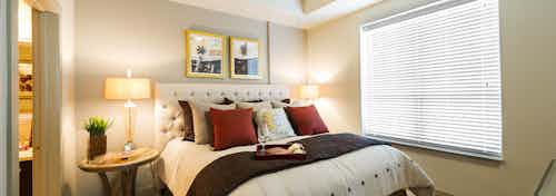 AMLI River Oaks apartment bedroom with bed with upholstered headboard, two nightstands with lamps and window with blinds