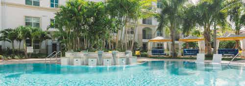 Daytime view of an AMLI Sawgrass Village swimming pool with cabanas, palm trees and a water feature cascading into the pool