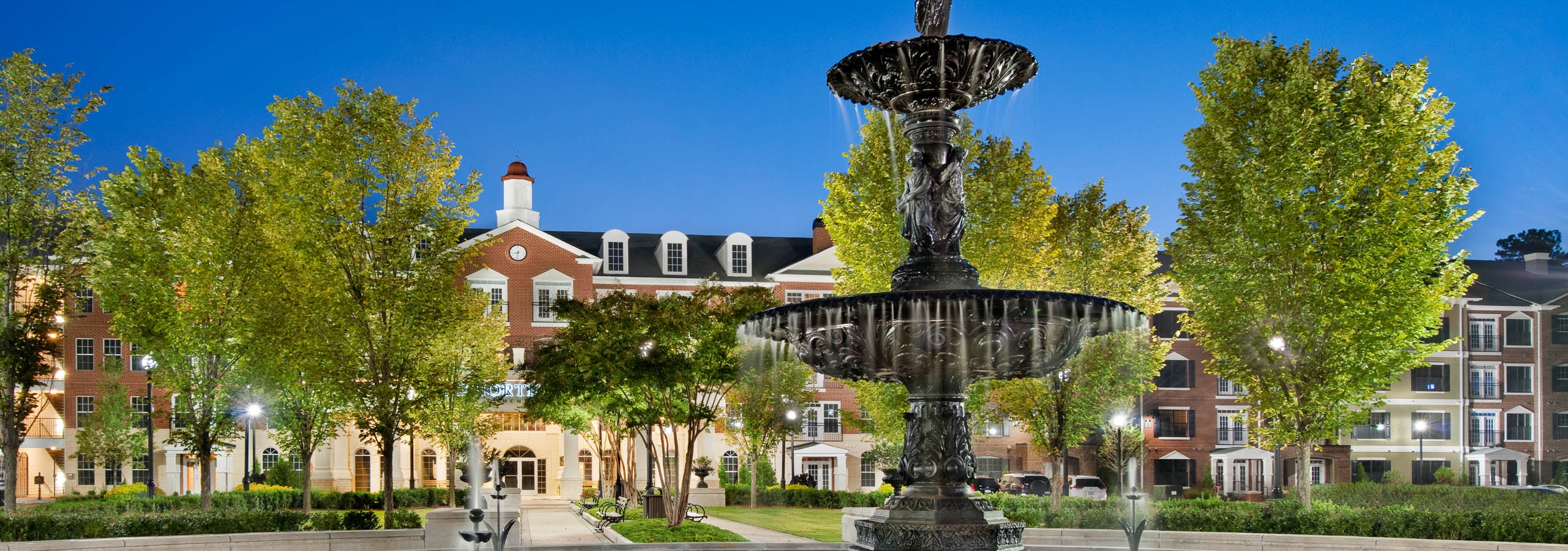 Exterior of AMLI North Point with brick facade and luscious trees surrounding a large fountain near the front of the building