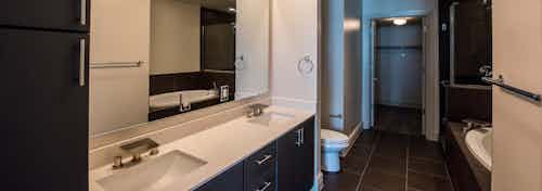 Interior view of AMLI Design District apartment bathroom with double vanity, oval garden tub, glass shower and closet