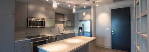 Interior of AMLI Design District apartment kitchen with gray cabinetry and pendant lights and stainless steel appliances