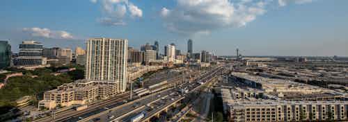 Daytime view of city of Dallas from AMLI Design District apartment building rooftop with blue sky and puffy clouds