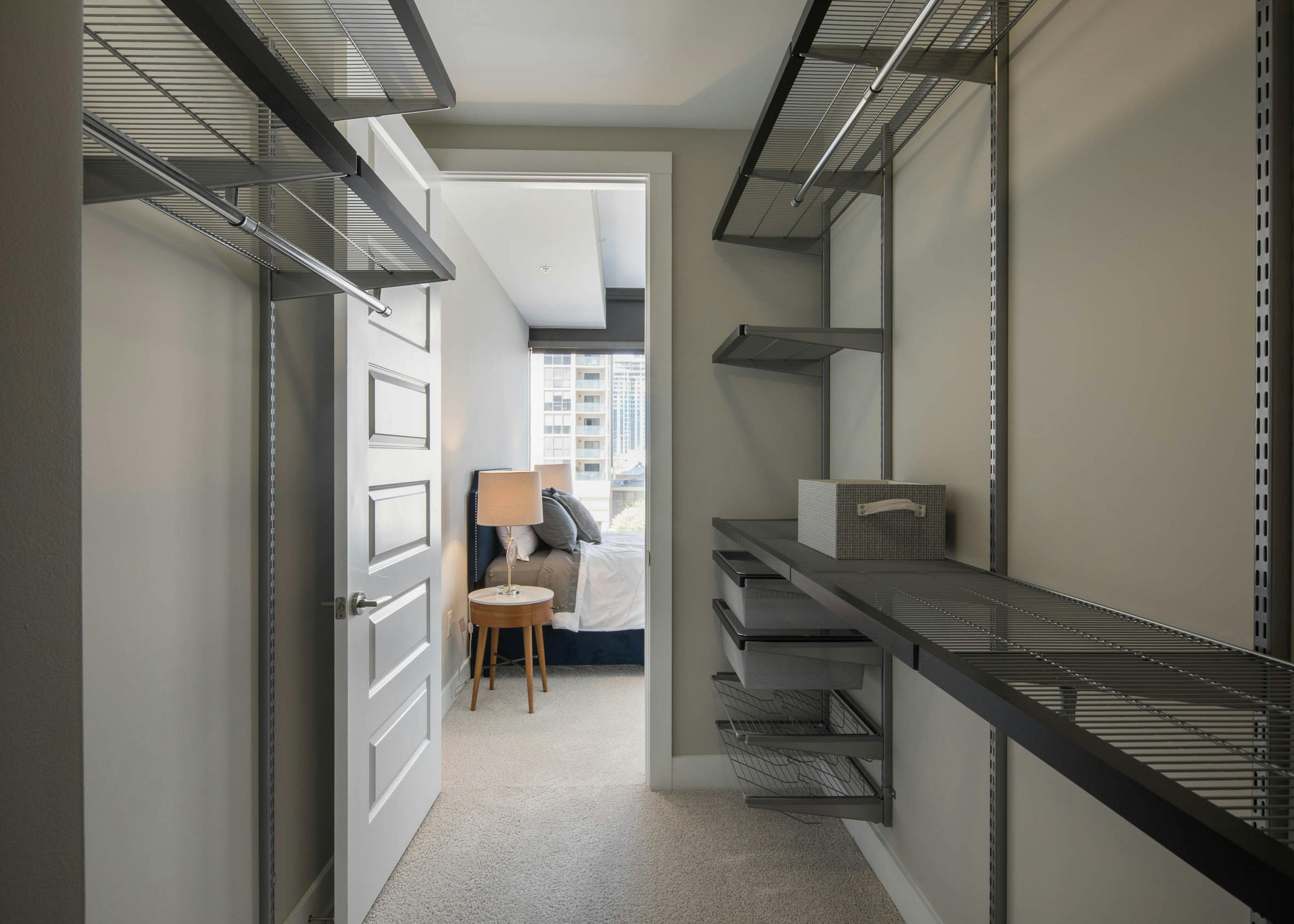 Interior of walk in closet at AMLI Arts Center with built in shelving and space to hang clothes with door opening to bedroom