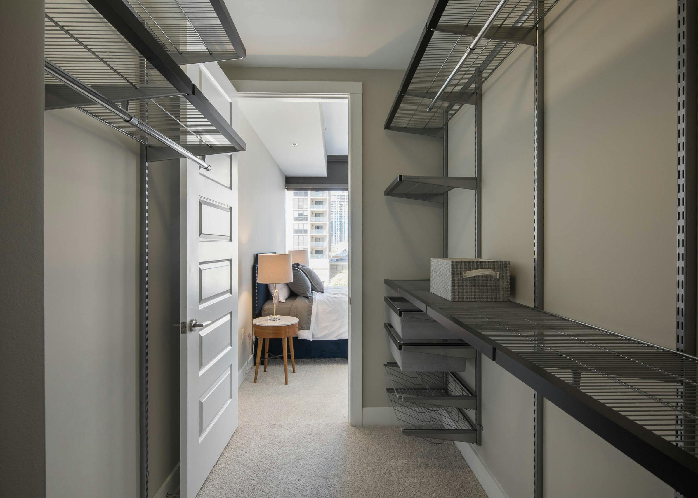 Interior of walk in closet at AMLI Arts Center with built in shelving and space to hang clothes with door opening to bedroom
