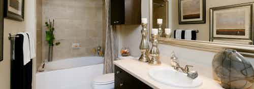 AMLI River Oaks apartment bathroom with granite vanity, large mirror, dark wood cabinets and garden tub with tile surround