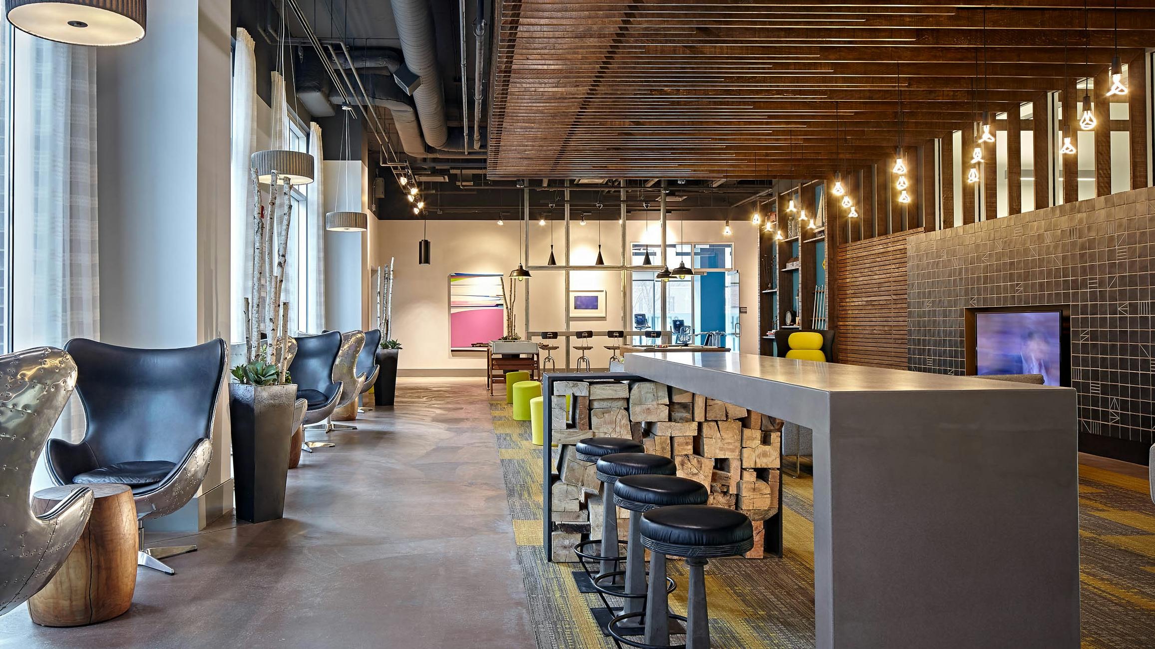 Lounge at AMLI Lofts which has bar stools and swivel chairs positioned by glass windows with hanging textured light fixtures