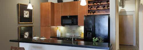 Interior view of AMLI Las Colinas apartment kitchen with black appliances, granite countertops and tile backsplash