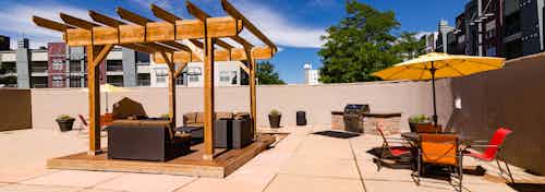 An outdoor picnic area with barbecues at AMLI Arista apartments with an awning as well as tables and chairs and an umbrella