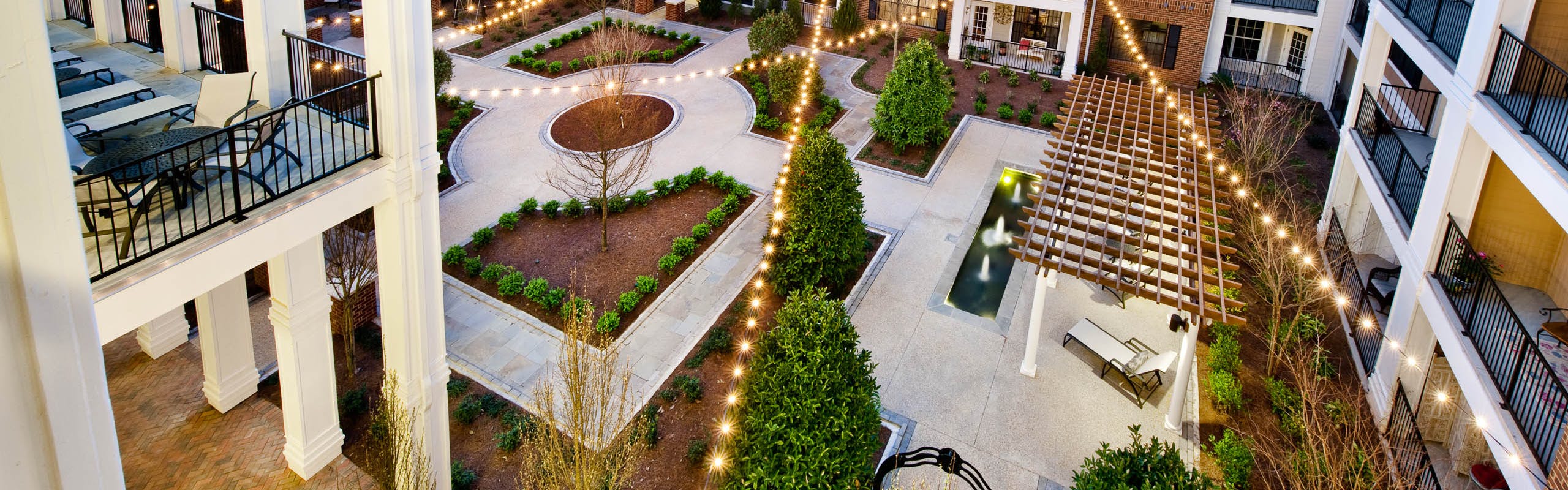 AMLI North Point courtyard with balconies and string lights above pavement for walking which is lined with pristine landscape