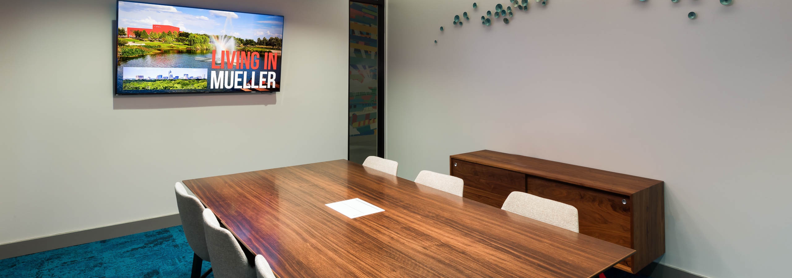 Interior view of conference room at AMLI on Aldrich with large wooden desk and a flat screen TV hanging on neutral wall