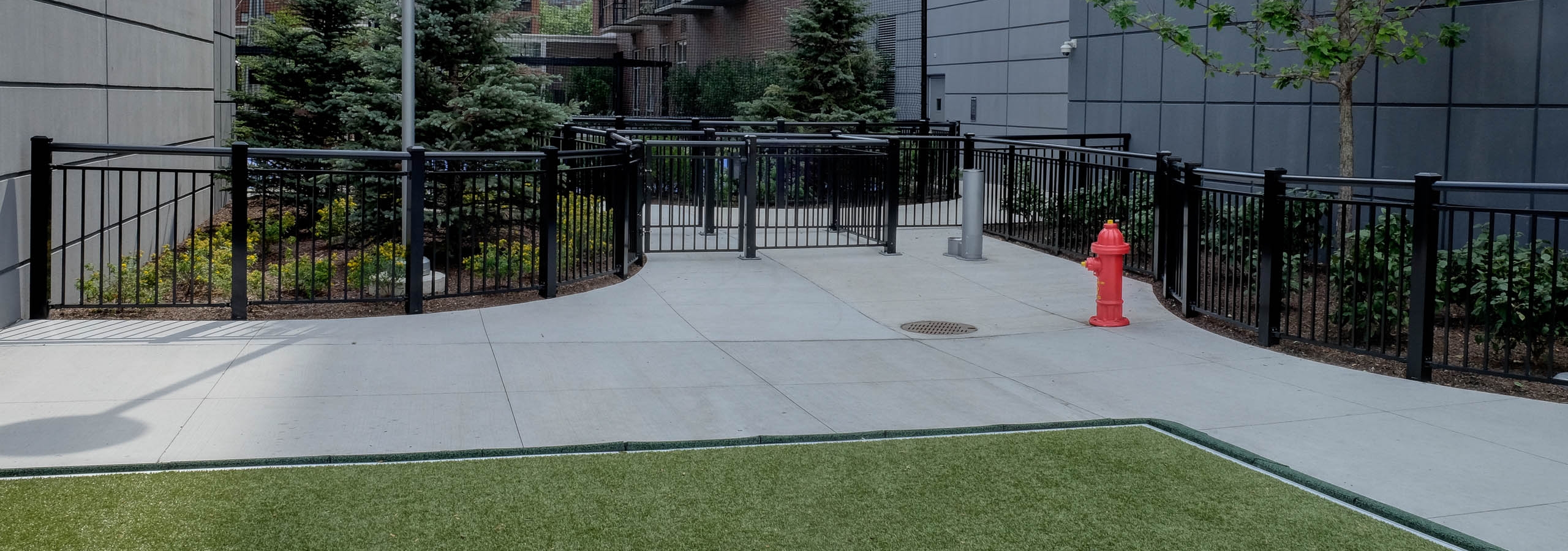 Exterior view of the gated dog run with artificial turf at the AMLI Lofts apartment community in the bright day time