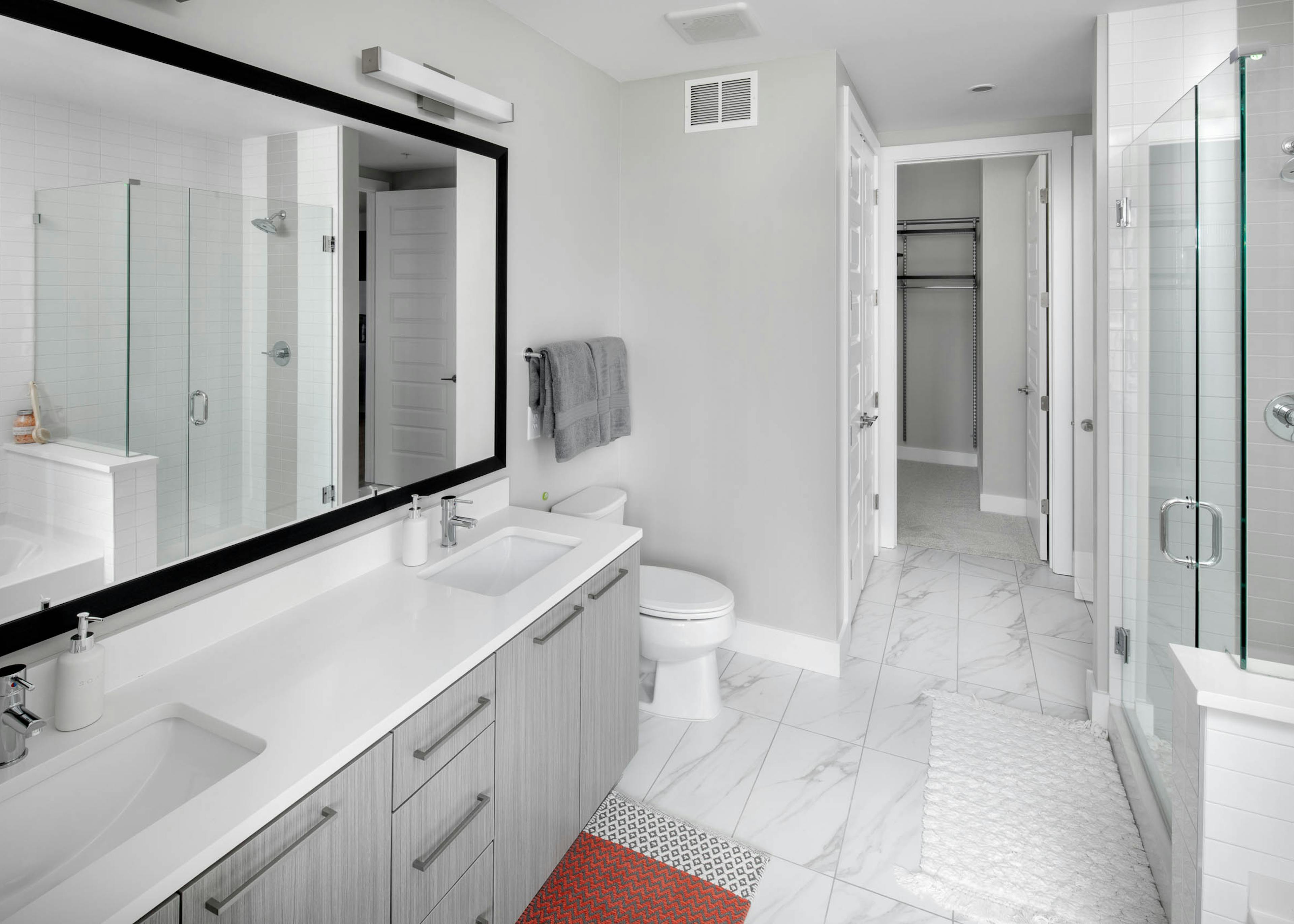AMLI Arts Center bathroom with a grey double vanity sink and glass door leading into shower with marble patterned floor tile