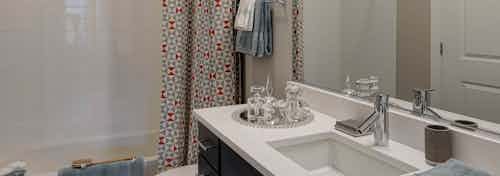 Interior view of a bathroom at AMLI Lofts with dark cabinets and a white countertop and bathtub with a patterned red curtain
