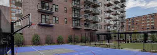 Exterior view of the sport court and multi-purpose green space at AMLI Lofts apartment community including a basketball hoop