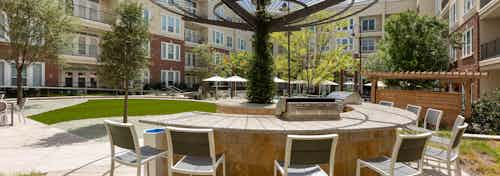 Daytime view of courtyard grill station at AMLI Frisco Crossing apartments with seating and pool area in background