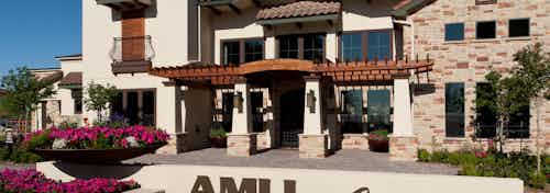 Daytime exterior of leasing office at AMLI at Escena apartment building with monument sign in foreground and pink flowers