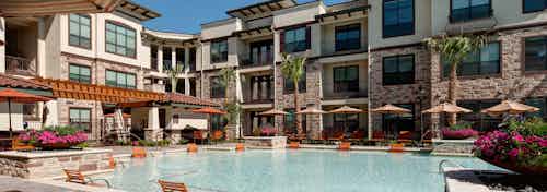 Daytime view of AMLI at Escena apartment building swimming pool with lounge seating in and out of water and umbrellas