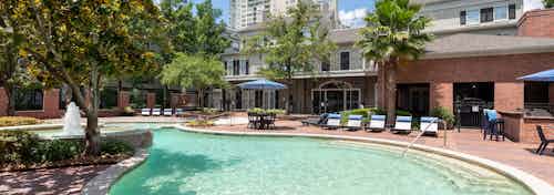Daytime exterior view of AMLI Memorial Heights swimming pool with lounge seating, umbrellas, grill station and trees