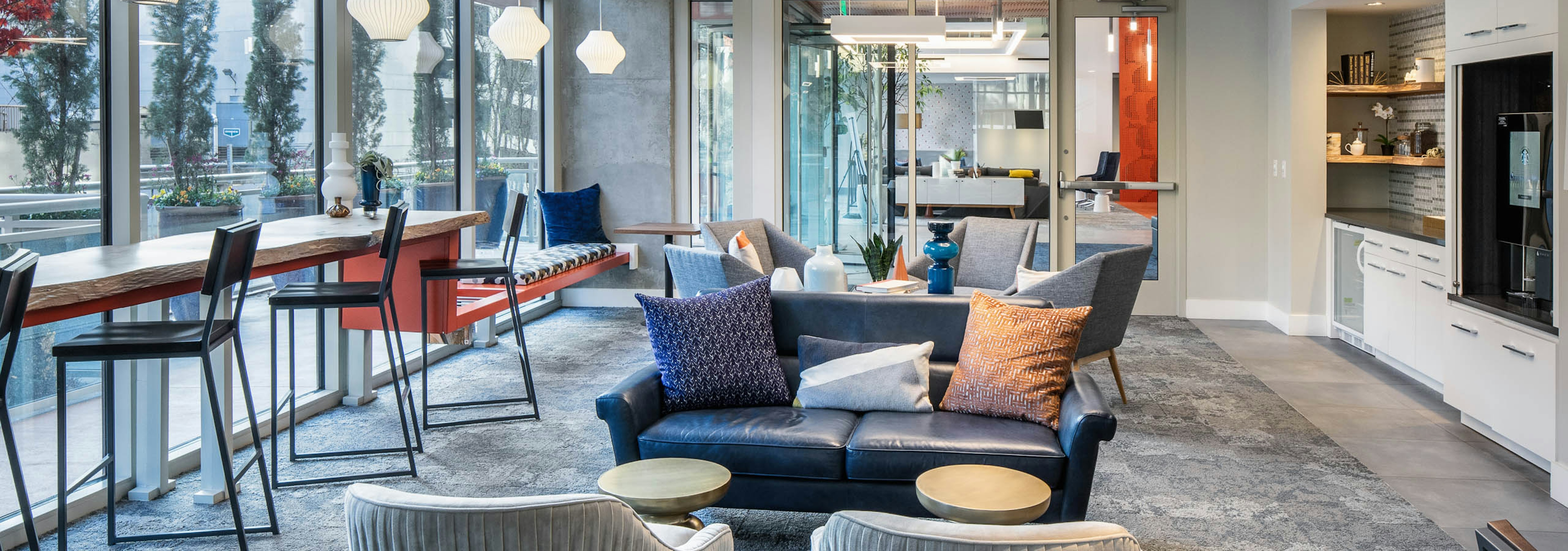 AMLI Arts Center clubroom with grey and blue seating and a white entertainment center with barstools facing tall windows