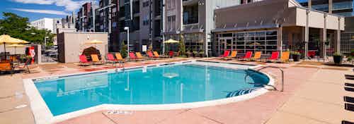 A daytime view of the pool at AMLI Arista apartments with several lounge chairs and umbrellas and a view of the clubhouse