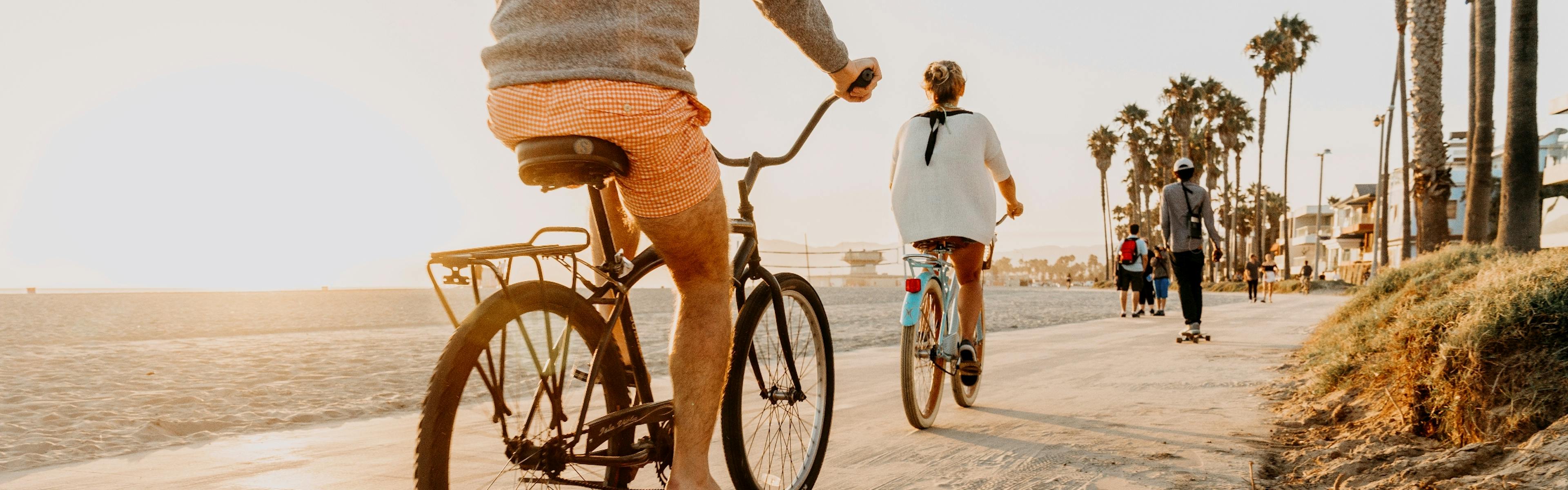 Lifestyle image of people riding bikes on a sidewalk in the sand along the beach