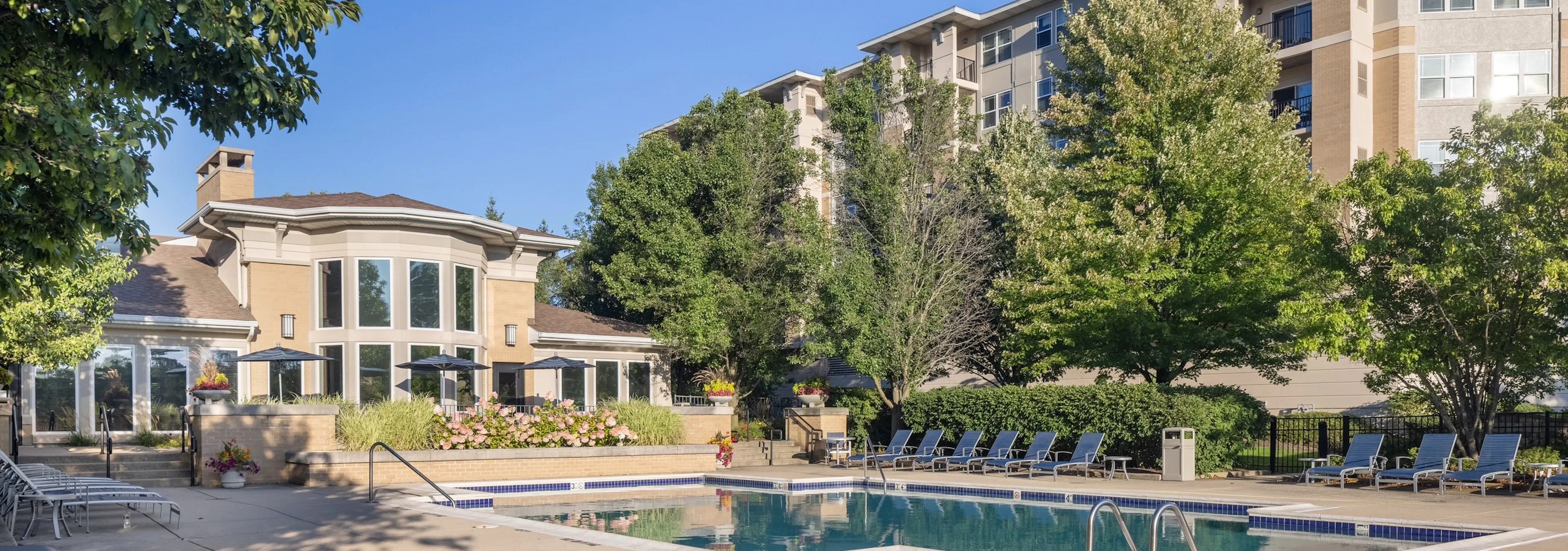 Exterior of the AMLI at Seven Bridges apartment building with behind a luxurious pool with blue lounge chairs and umbrellas
