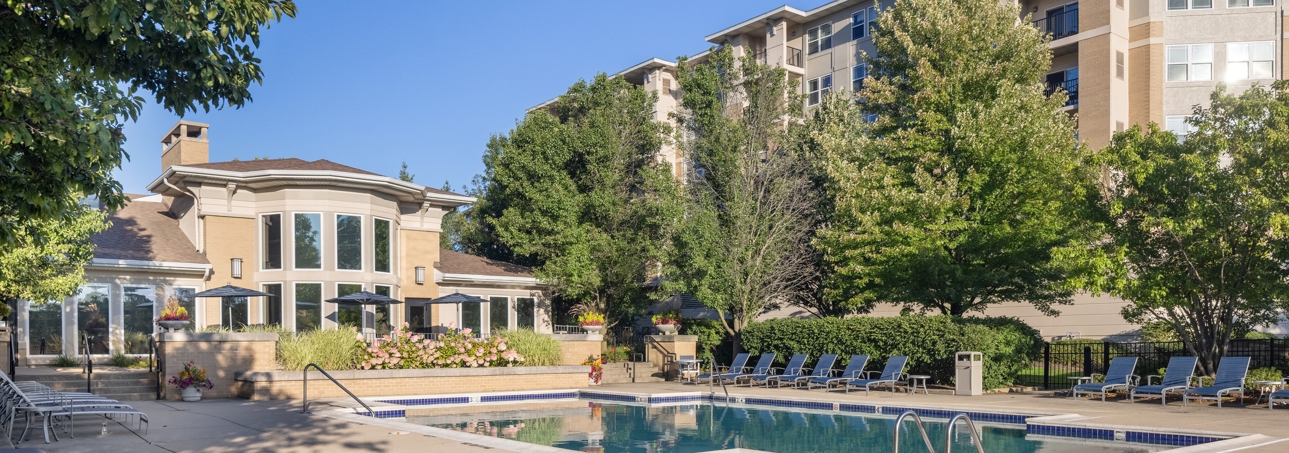 Exterior of the AMLI at Seven Bridges apartment building with behind a luxurious pool with blue lounge chairs and umbrellas