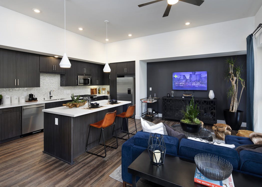 Interior of AMLI Marina Del Rey kitchen island with fully set quartz countertop, dark cabinets and blue sofa in living room