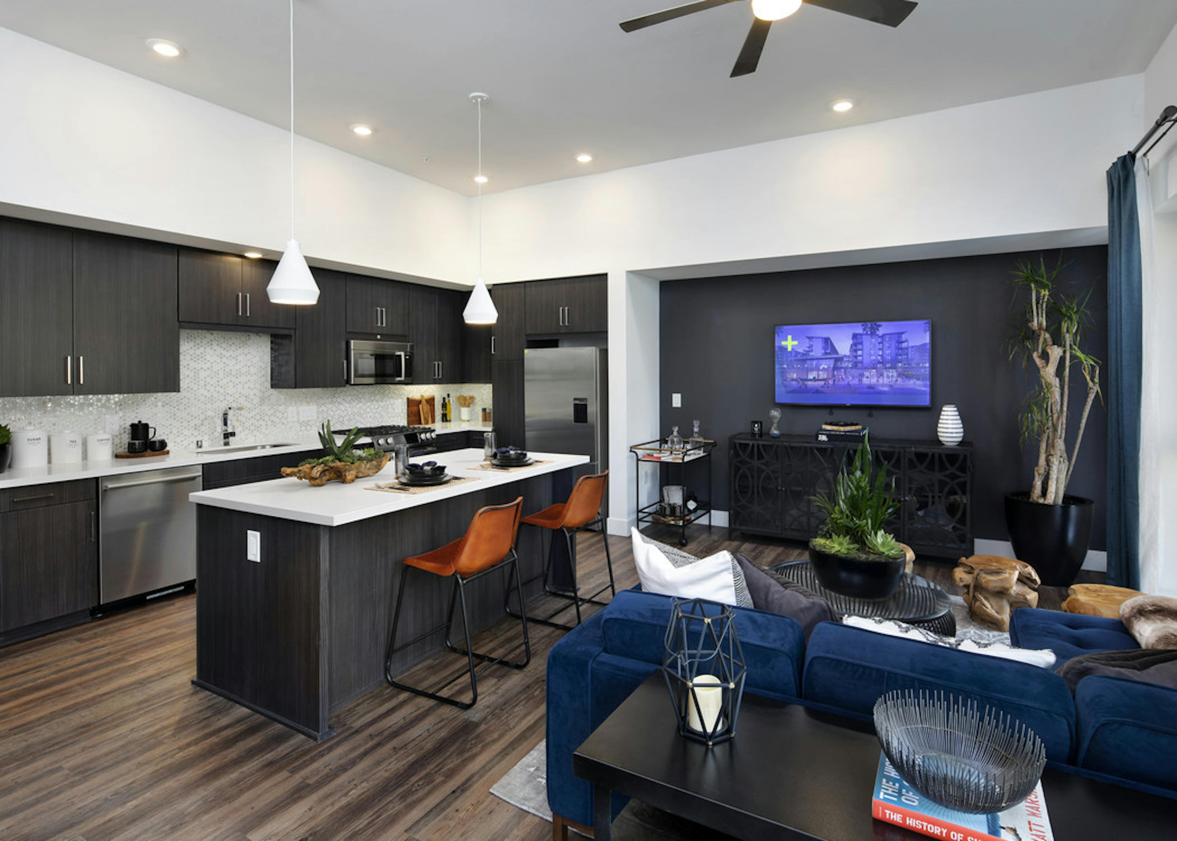 Interior of AMLI Marina Del Rey kitchen island with fully set quartz countertop, dark cabinets and blue sofa in living room