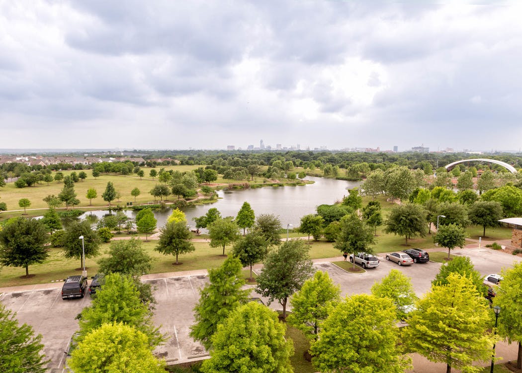 View of AMLI Mueller Lake Park with lake and surrounding green foliage under a cloudy blue sky