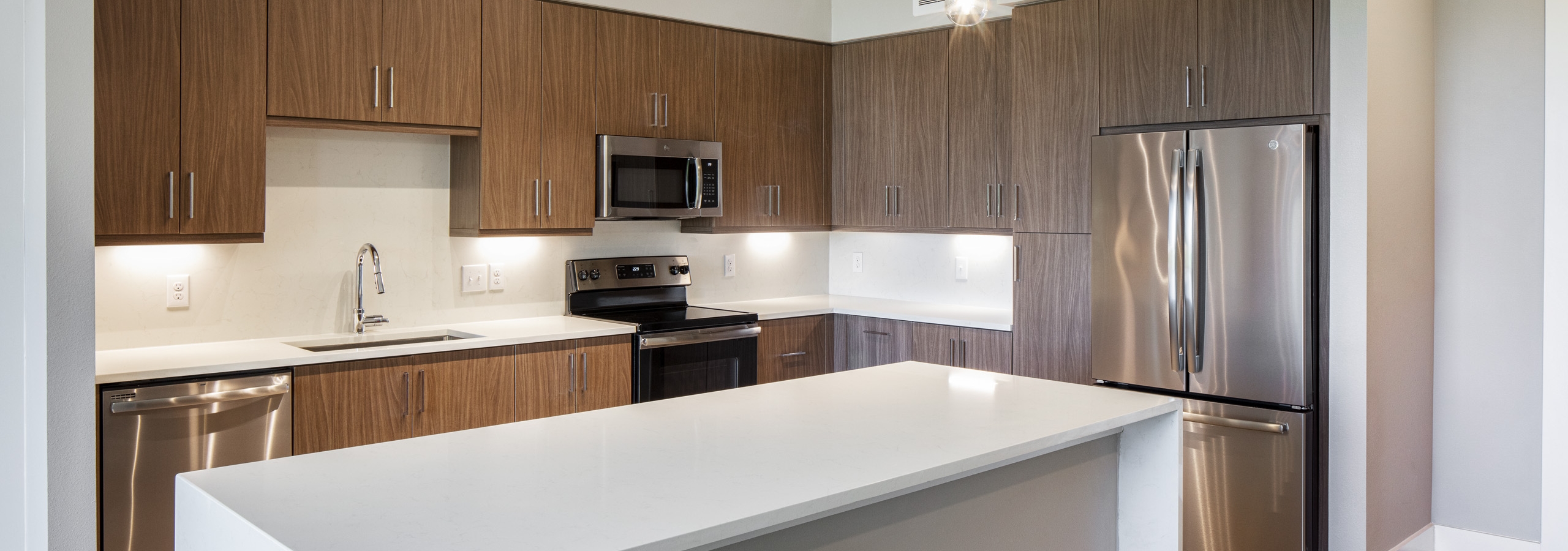 AMLI South Shore kitchen with white quartz island with waterfall edge and dark wood cabinets with stainless steel appliances