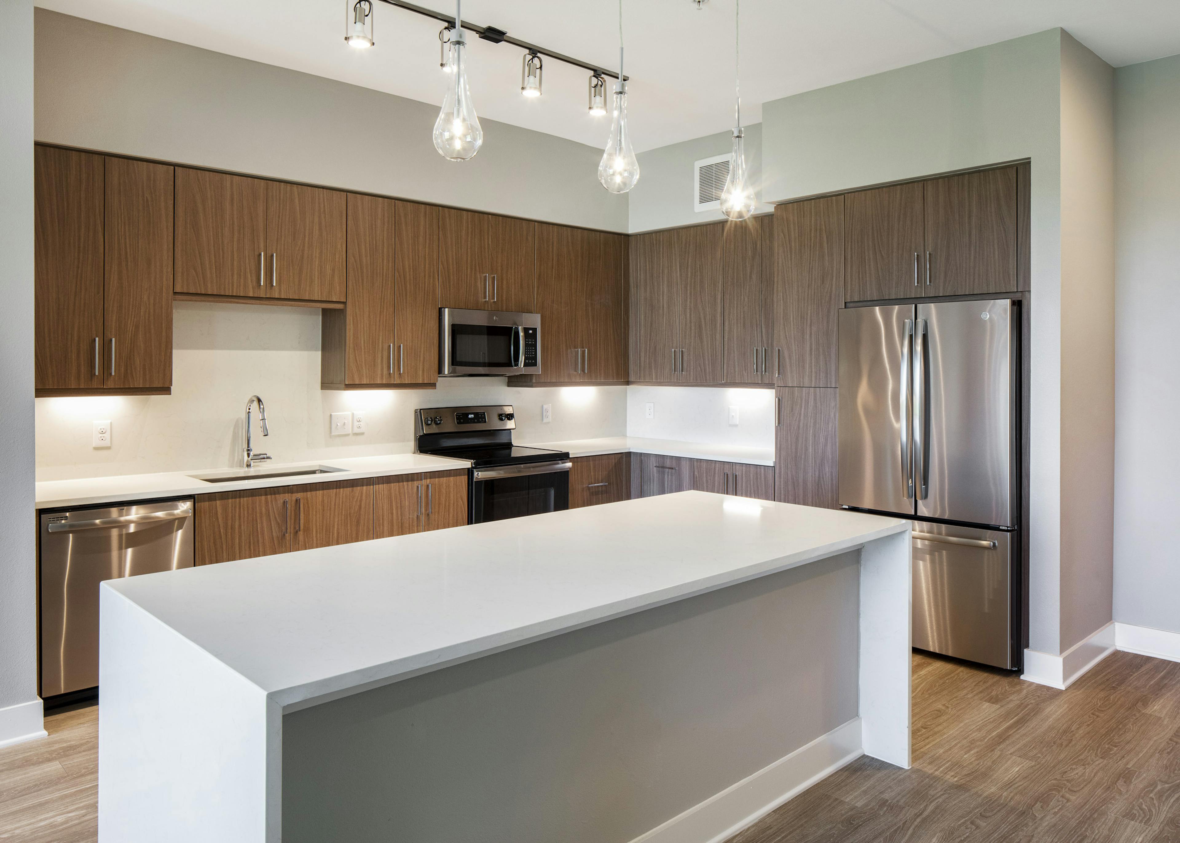 AMLI South Shore kitchen with white quartz island with waterfall edge and dark wood cabinets with stainless steel appliances