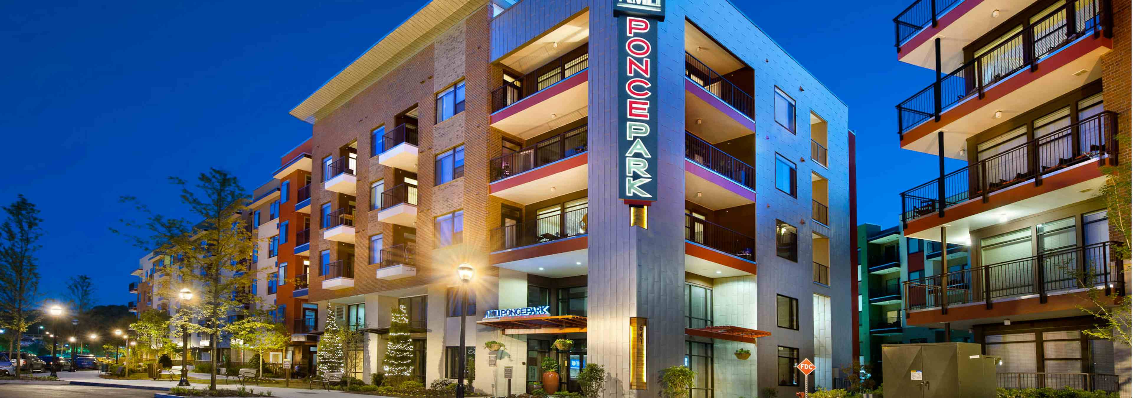 Nighttime exterior view of AMLI Ponce Park apartment community brick facade with sign above building entrance and trees