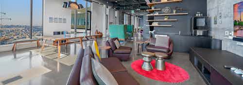 Game room at AMLI Arc apartment building with brown leather seating facing TV and ping pong table and wall of windows in rear