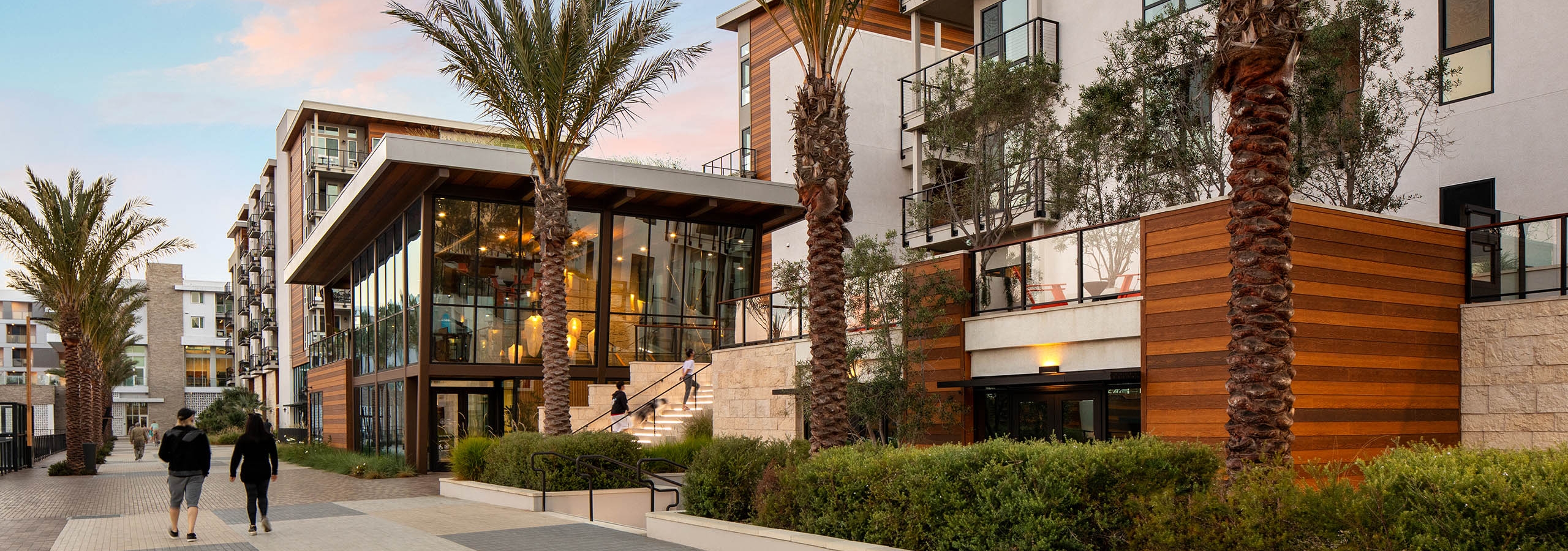 A couple walking at dusk along the promenade towards the Jewel building with palm trees at AMLI Marina Del Rey apartments
