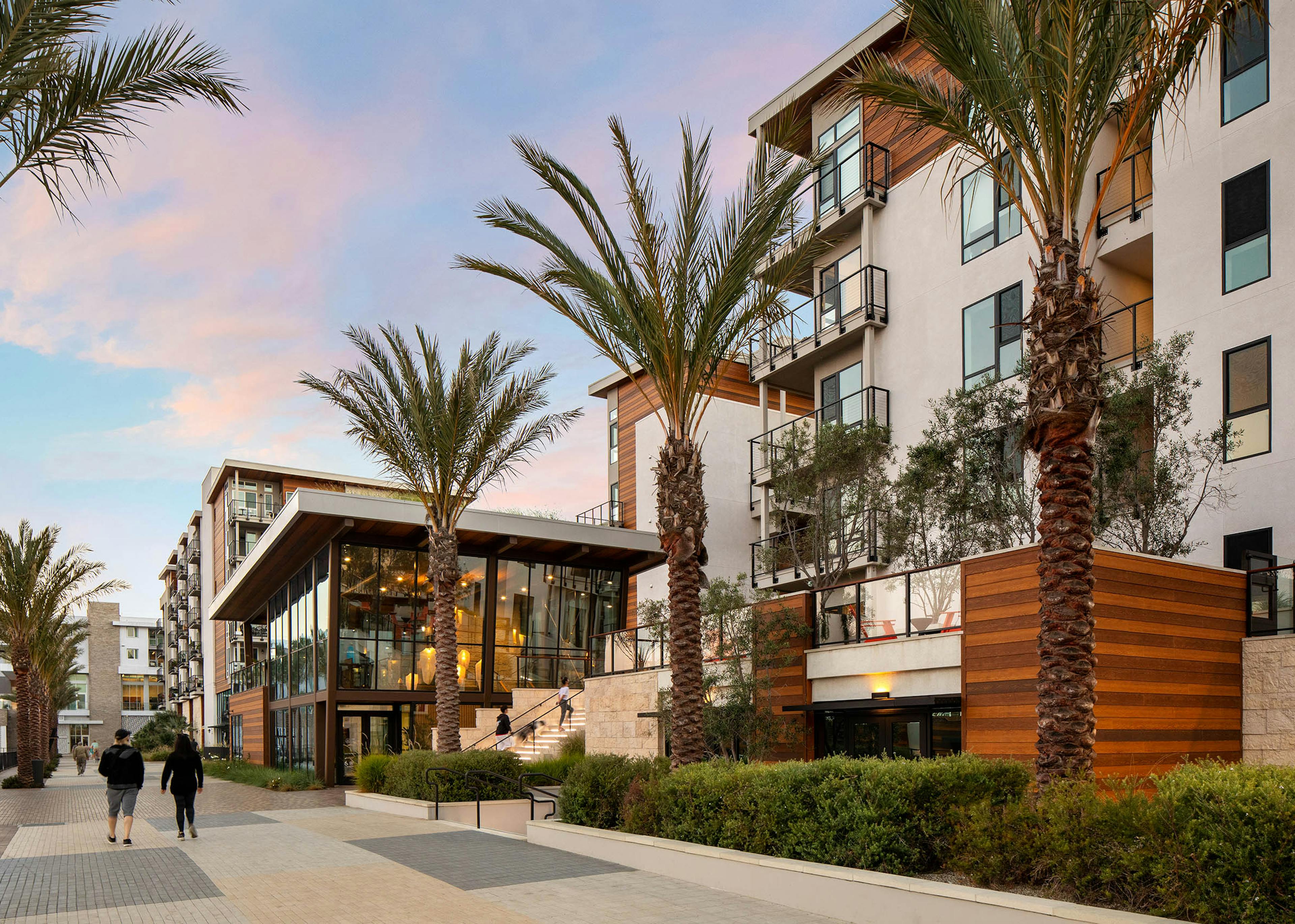 A couple walking at dusk along the promenade towards the Jewel building with palm trees at AMLI Marina Del Rey apartments