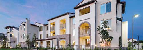 Exterior dusk rendering of AMLI Spanish HIlls apartment building with lit patios and arched entry ways surrounded by greenery