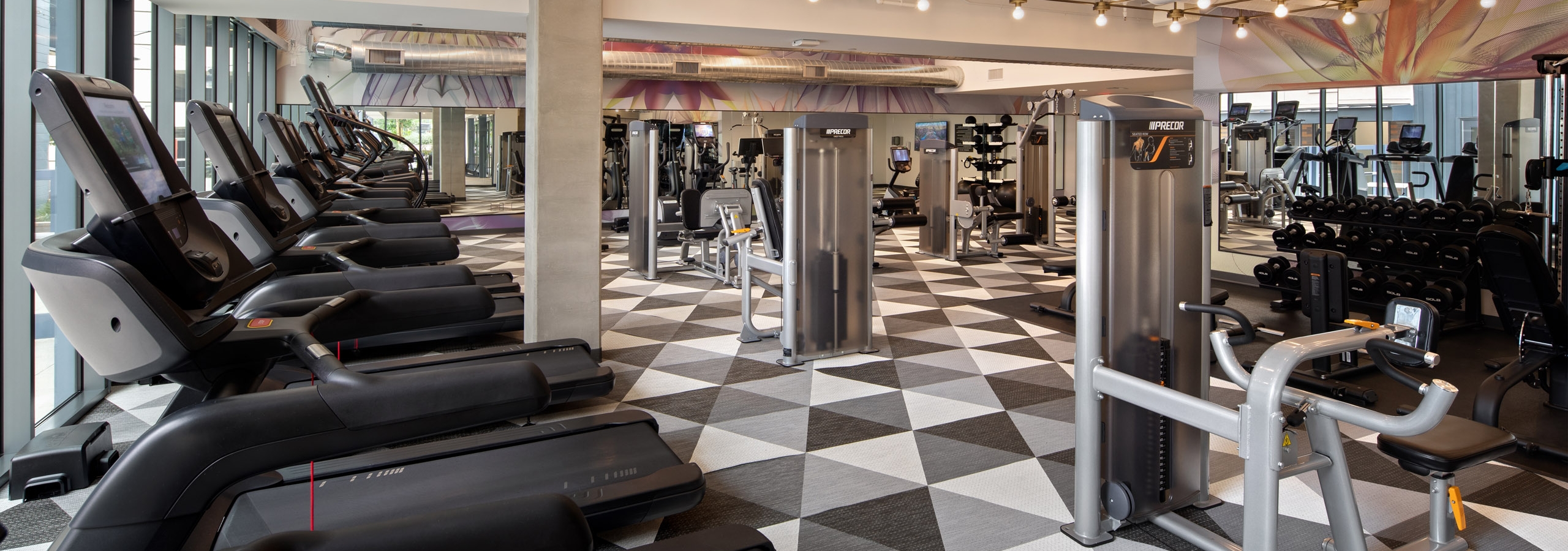 Interior view of fitness center with several cardio machines on custom checkered flooring at AMLI Old Pasadena apartments