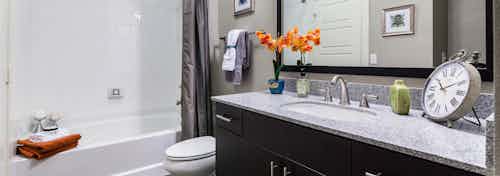 Interior view of AMLI Arista apartment bathroom and steel fixtures and large mirror and clock as well as stylish artwork