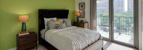 An AMLI 900 apartment bedroom with vibrant decor accents and large glass doors leading to a balcony with city views