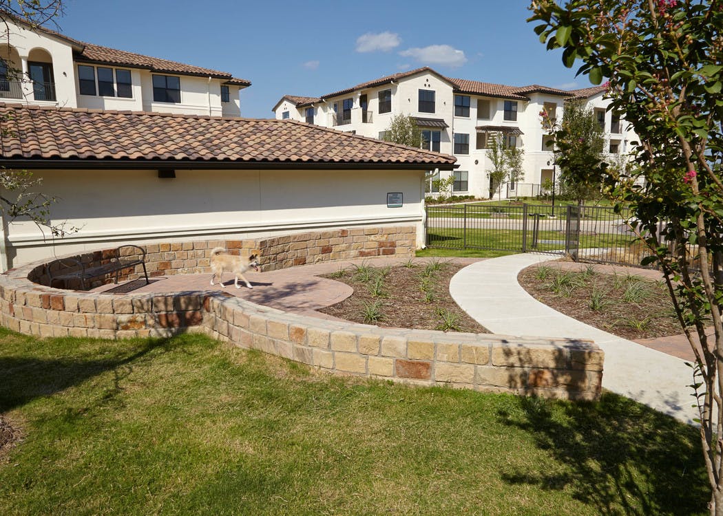 Paw park at AMLI on Riverside with a paved walking path and green grass with short brick ledges and a small dog walking