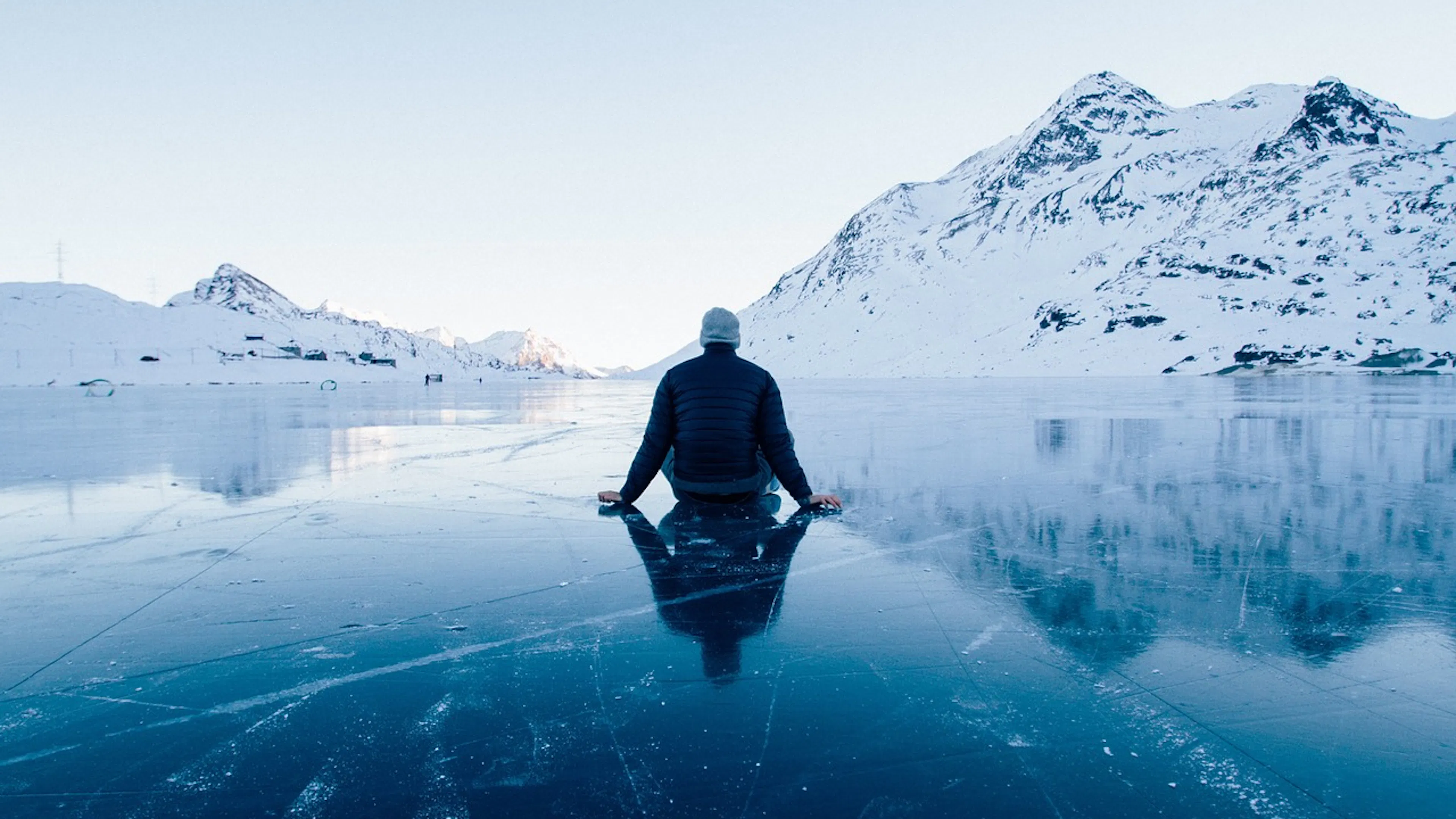 man sitting cross-legged on frozen lake with snow covered mountains in background