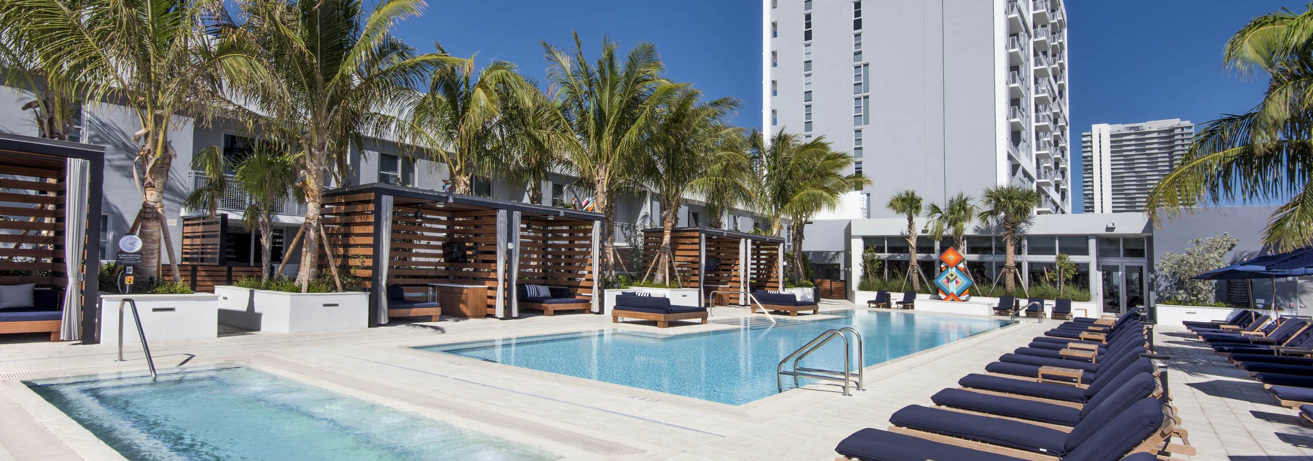 AMLI Midtown 29 apartments pool and spa with individual wood slat cabanas and navy lounge chairs with palm trees