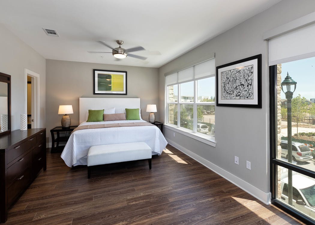 Interior of AMLI on Aldrich bedroom with a large white bed near windows with daytime scenic view and dark wood flooring