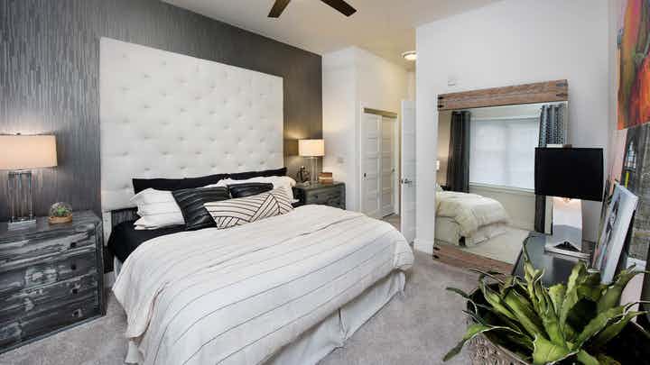 AMLI Buckhead bedroom with carpet and light walls with a tall ivory headboard and matching bedding with black throw pillows