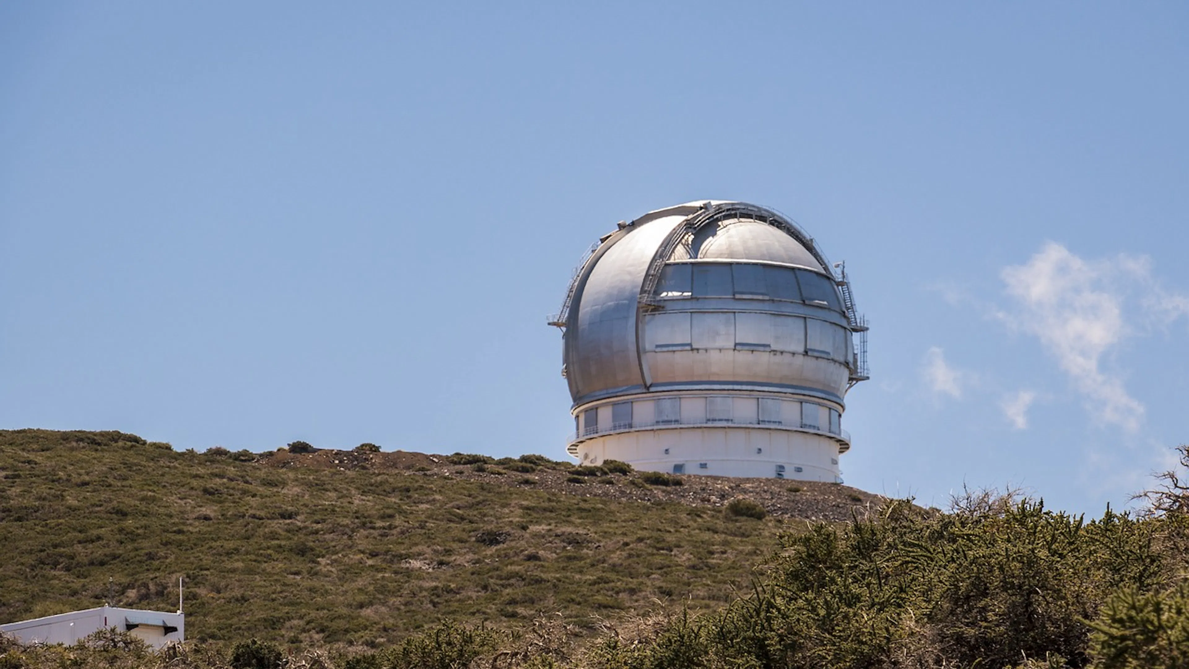 A silver observatory on the top of a desert hill against a blue sky