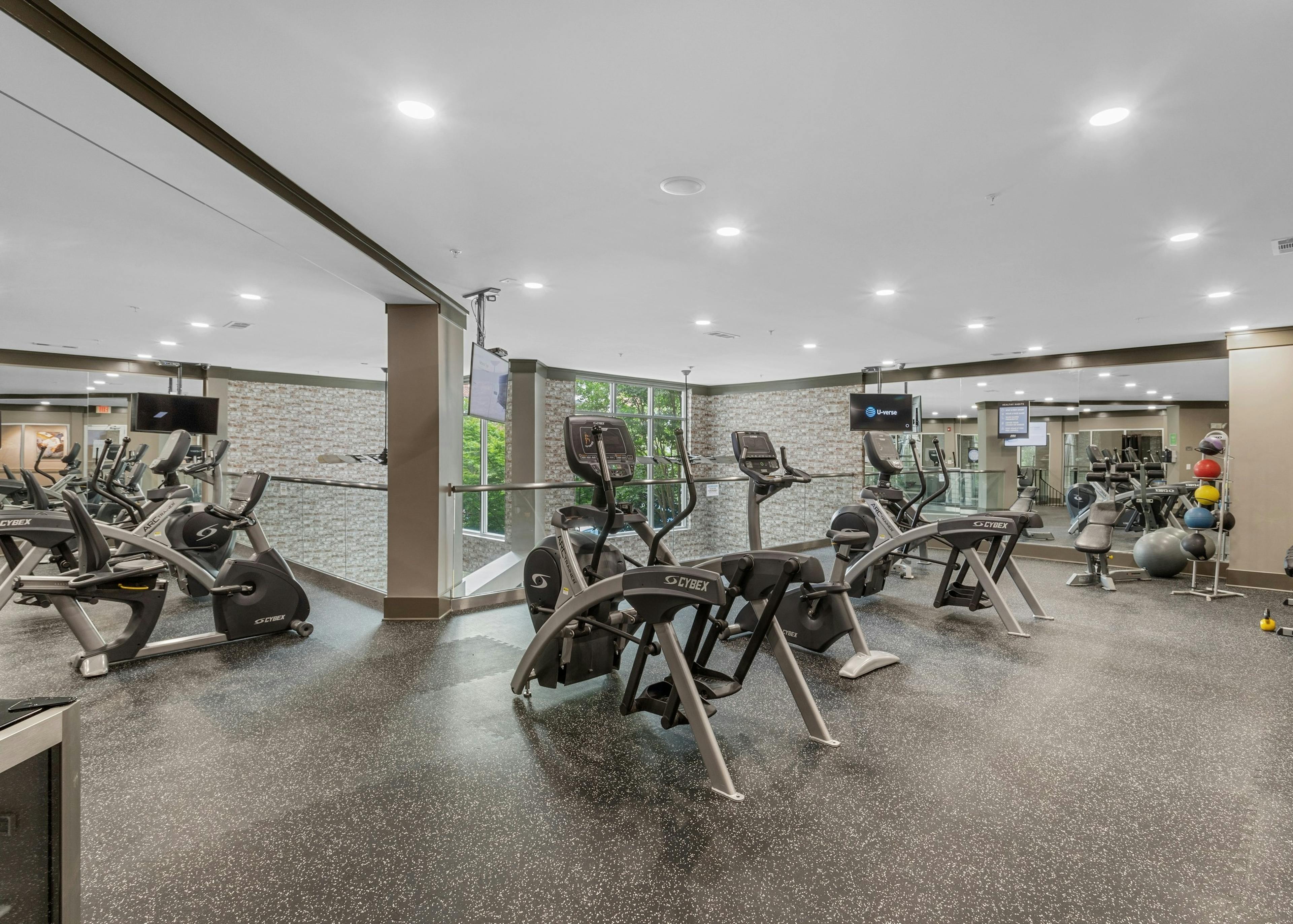 The fitness center at AMLI North Point with speckled floors and exercise equipment with hanging TVs and a full mirror wall 